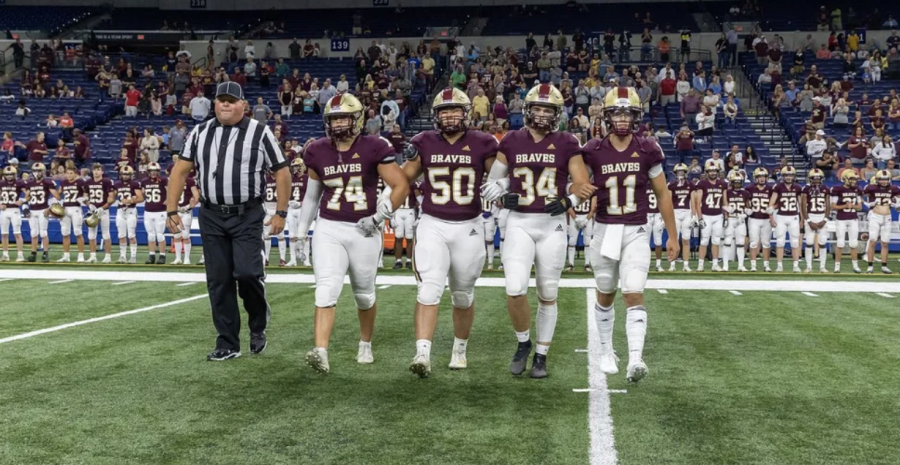 Logan Petrie 23, Conway Zhang 23, Cole Williams 23, and Nolan Buckman 23 take the field with their arms locked for the coin toss.